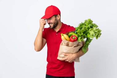 Sakallı genç adam elinde sebze dolu bir çanta beyaz arka planda izole edilmiş gülüyor.