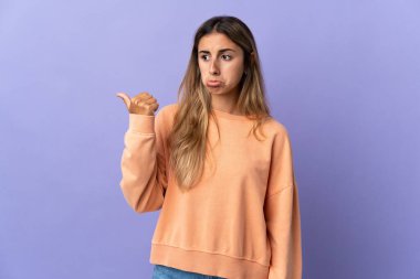 İzole edilmiş mor arka planı olan genç İspanyol kadın mutsuz ve bir tarafı işaret ediyor.