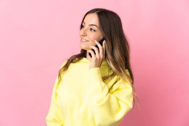 Pembe arka planda izole edilmiş genç Romen kadın cep telefonuyla biriyle sohbet ediyor