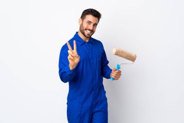Beyaz arka planda izole edilmiş boya silindiri tutan ressam gülümsüyor ve zafer işareti gösteriyor.