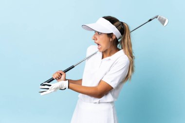 Genç İspanyol golfçü kadın, yalıtılmış mavi duvarın üzerinden bakarken sürpriz bir ifadeyle.