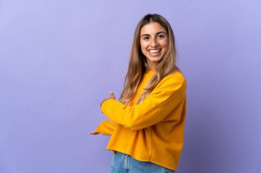 İzole edilmiş mor arka planda genç bir İspanyol kadın davet etmek için ellerini yana uzatıyor.