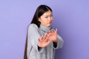 Asyalı genç bir kadın soyutlanmış arka planda sinirleri gergin, ellerini öne uzatıyor.