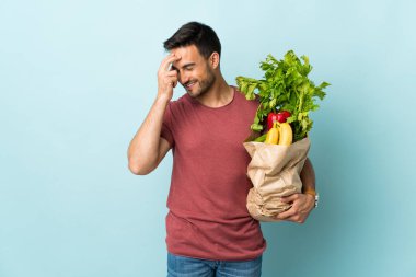 Mavi arka planda izole edilmiş sebze alan genç beyaz adam gülüyor.