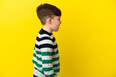 Küçük kızıl saçlı çocuk sarı arka planda izole edilmiş. Yan pozisyonda gülüyor.