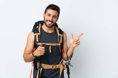 Genç dağcı, büyük bir sırt çantası ve beyaz arka planda izole edilmiş yürüyüş direkleri ile parmağı yan tarafı işaret ediyor.