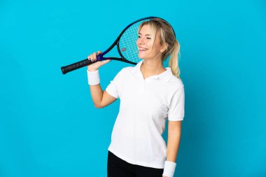 Genç Rus kadın mavi arka planda izole edilmiş tenis oynuyor ve yukarı bakıyor.