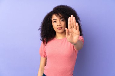 Mor arka planda izole edilmiş genç Afrikalı Amerikalı kadın dur hareketi yapıyor.