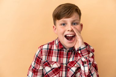 Bej arka planda izole edilmiş küçük kızıl saçlı çocuk.