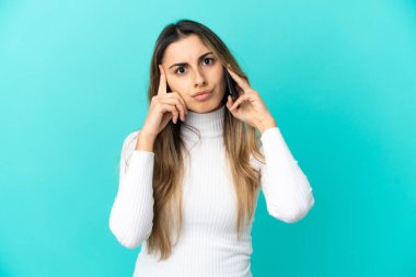 Mavi arka planda izole edilmiş cep telefonu kullanan beyaz bir kadın bir fikir düşünüyor.