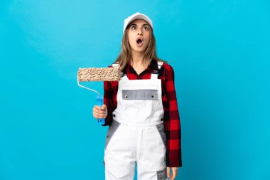 Ressam kadın izole edilmiş mavi arka planda yukarı bakıyor ve şaşırmış bir ifadeyle