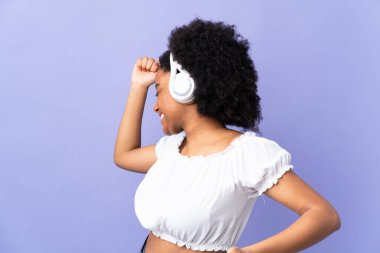 Genç Afrikalı Amerikalı kadın mor arka planda izole edilmiş müzik ve dans dinliyor.