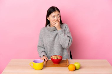 Genç Çinli kız kahvaltı yapıyor. Yan tarafa bakarken sürpriz jest yapıyor.