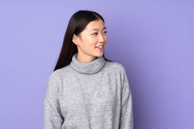 Asyalı genç bir kadın soyutlanmış arka planda, yana bakıyor ve gülümsüyor.