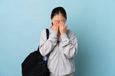 Spor çantasıyla genç bir Çinli kadın izole edilmiş mavi arka planda yorgun ve hasta bir ifadeyle.