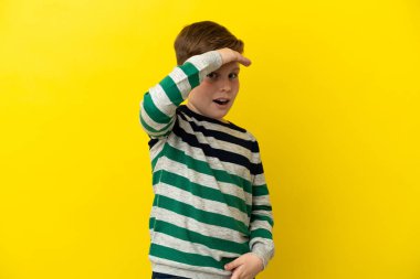 Küçük kızıl saçlı çocuk sarı arka planda izole edilmiş. Önüne bakarken sürpriz jest yapıyor.