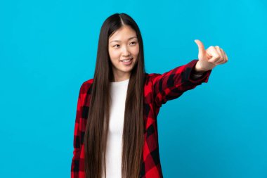 Soyutlanmış mavi arka planda genç bir Çinli kız baş parmak işareti yapıyor.