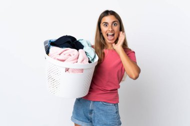 Beyaz arka planda, şaşırmış ve şok olmuş bir yüz ifadesiyle izole edilmiş çamaşır sepeti tutan genç bir kadın.