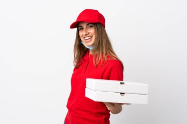 Pizza teslimatı yapan kadın elinde pizza tutuyordu. Koronavirüsten koruyordu. İzole edilmiş beyaz bir duvarın üzerinde bir maskeyle gülümsüyordu.