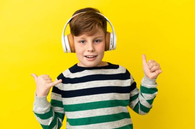 Küçük kızıl saçlı çocuk sarı arka planda izole edilmiş rock hareketleri yapan müzik dinliyor.