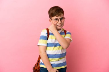 Küçük kızıl saçlı beyaz çocuk pembe arka planda izole edilmiş zaferi kutluyor.