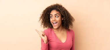 Genç Afrikalı Amerikalı bir kadın bej arka planda izole edilmiş. Çözümün farkına varmak için parmağını kaldırıyor.