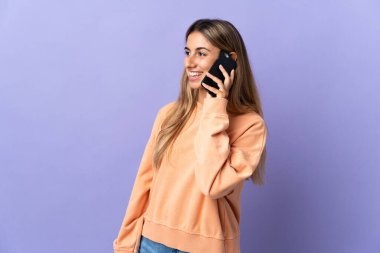 İzole edilmiş mor arka planda genç bir İspanyol kadın cep telefonuyla sohbet ediyor.