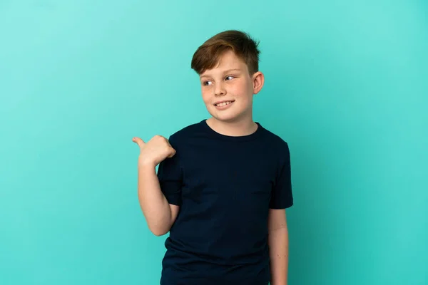 Kleine Roodharige Jongen Geïsoleerd Blauwe Achtergrond Wijzend Naar Zijkant Een — Stockfoto