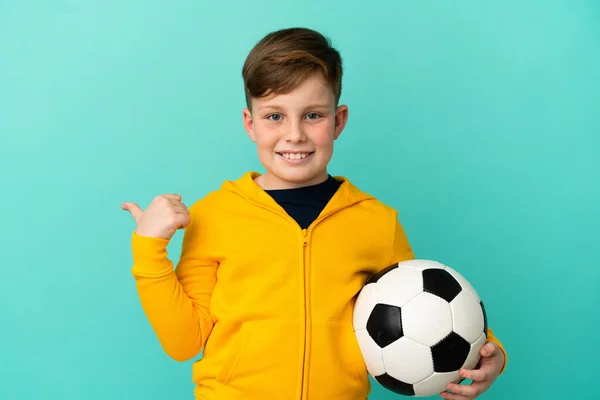 Roodharige Kind Spelen Voetbal Geïsoleerd Blauwe Achtergrond Wijzend Naar Zijkant — Stockfoto