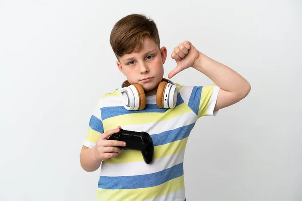 一个红头发的小男孩拿着一个白色背景的游戏垫 带着负面表情垂下大拇指 — 图库照片