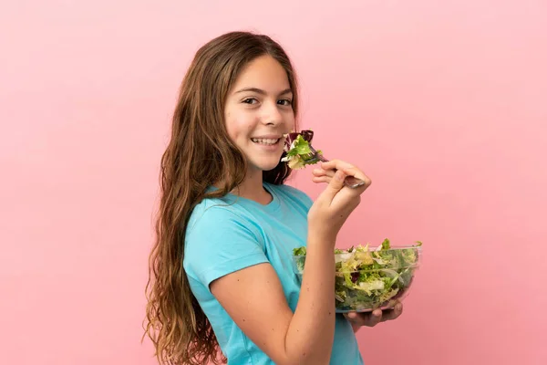 一个被粉色背景隔离的高加索小女孩手里拿着一碗带着快乐表情的沙拉 — 图库照片