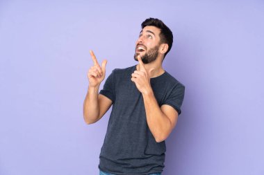 Beyaz tenli yakışıklı adam işaret parmağıyla işaret ediyor. İzole edilmiş mor arka plan üzerinde harika bir fikir.