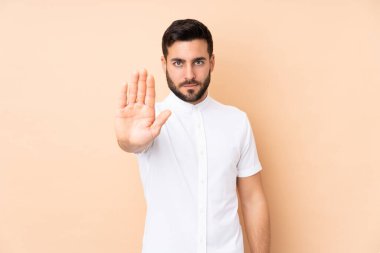 Beyaz tenli yakışıklı adam, bej arka planda izole edilmiş. Durdurma hareketi yapıyor.