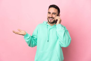Beyaz tenli yakışıklı adam pembe arka planda izole edilmiş cep telefonuyla sohbet ediyor.