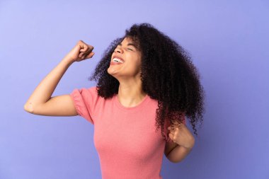 Mor arka planda izole edilmiş genç Afrikalı Amerikalı kadın zaferi kutluyor.