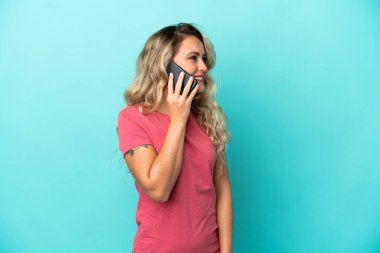 Mavi arka planda izole edilmiş genç Brezilyalı bir kadın cep telefonuyla biriyle sohbet ediyor.