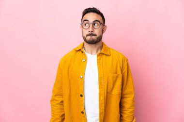 Pembe arka planda izole edilmiş beyaz, yakışıklı genç bir adam yukarı bakarken şüphe duyuyor.