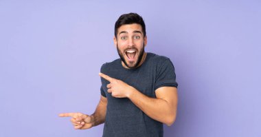 Kafkas yakışıklı adam şaşırdı ve yalıtılmış mor arka plan üzerinde işaret ediyor.