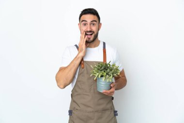 Bahçıvan beyaz arka planda saklanmış bir bitki tutuyor. Şaşırmış ve şok olmuş bir yüz ifadesi var.