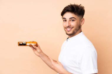 Arap adam bej arka planda izole edilmiş suşi yiyor ve onu işaret ediyor.