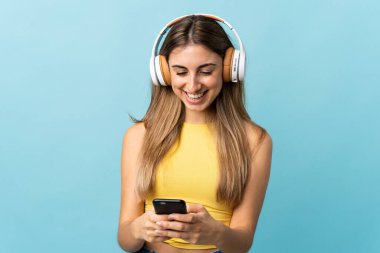 Soyutlanmış mavi arka plan müzik dinleyen ve cep telefonu arayan genç bir kadın.