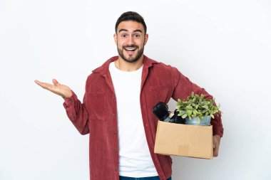 Beyaz arka planda izole edilmiş, şok olmuş yüz ifadesi olan şeylerle dolu bir kutuyu kaldırırken genç beyaz bir adam hamle yapıyor.