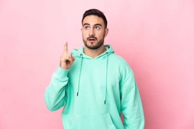 Pembe arka planda izole edilmiş beyaz, yakışıklı genç bir adam bir fikir düşünüyor.
