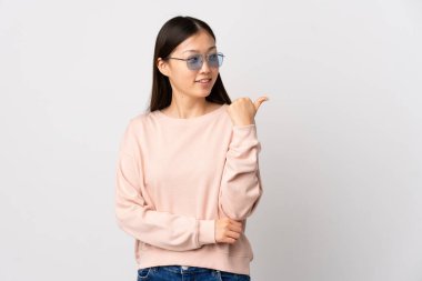 İzole edilmiş beyaz arka planı olan genç bir Çinli kız bir ürün sunmak için kenarı işaret ediyor.