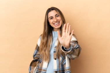 Beyazlı genç bir kadın bej arka planda izole edilmiş. Beş parmaklı sayıyor.