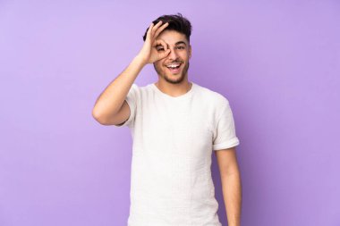 İzole edilmiş arka planda yaşayan Arap yakışıklı adam parmaklarıyla tamam işareti gösteriyor.