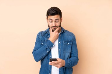 Beyaz tenli yakışıklı adam bej arka planda izole edilmiş düşünüyor ve bir mesaj gönderiyor.