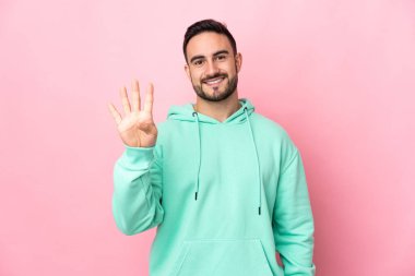 Beyaz tenli yakışıklı adam pembe arka planda izole edilmiş mutlu ve parmaklarıyla dört kişi sayıyor.