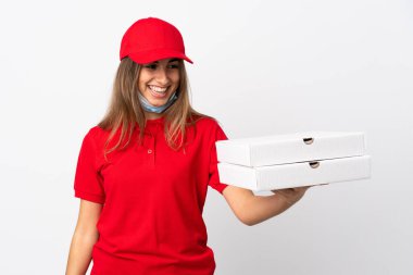 Pizza teslimatçısı kadın elinde pizza tutuyordu. Koronavirüsten koruyordu. İzole edilmiş beyaz bir maskeyle mutlu bir ifadeyle.