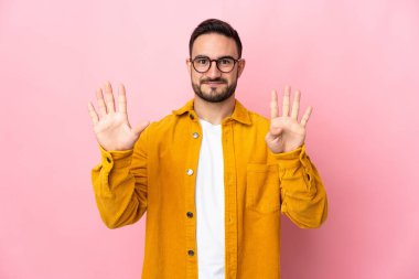 Pembe arka planda izole edilmiş beyaz, yakışıklı genç adam parmaklarıyla dokuza kadar sayıyor.